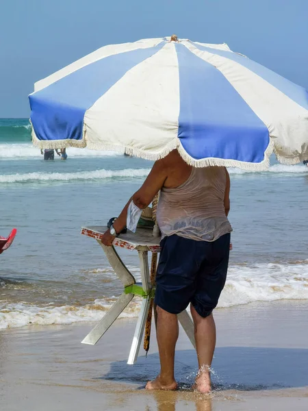 Masasını şemsiyeyle tutan ve kıyıya doğru yürüyen tanınmamış bir adam.