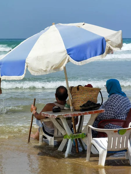 Koca ve karısı yaz tatili boyunca okyanus suyunda sandalyelerinde dinleniyorlar.