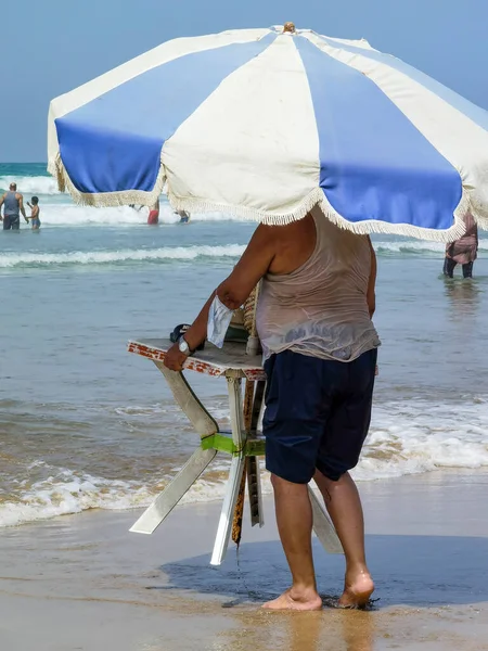 Masasını şemsiyeyle tutan ve kıyıya doğru yürüyen tanınmamış bir adam.