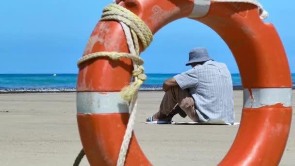 Ensam Man Sitter Ensam Stranden Och Inramad Räddnings Orange Ring — Stockvideo