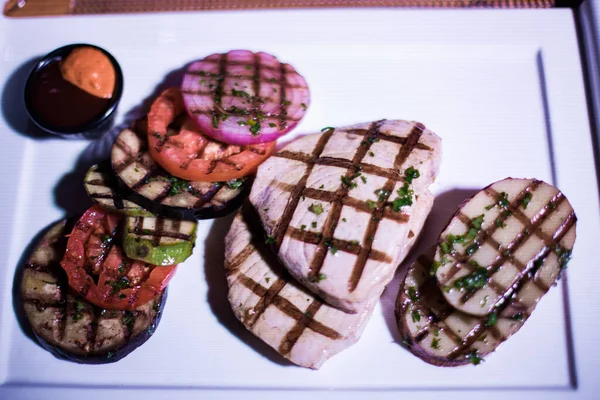 Bir tabak ızgara tavuk göğsü. Izgara patates, domates ve soğan.