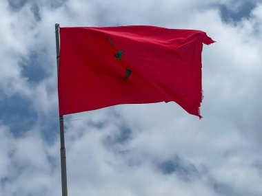 Arka planda bulutlu bir gökyüzü dalgalanan Fas bayrağı