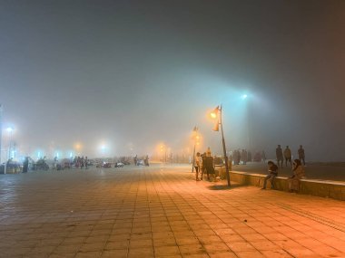 Sisli bir gecede halka açık bir meydanda yürüyen bir kalabalık.