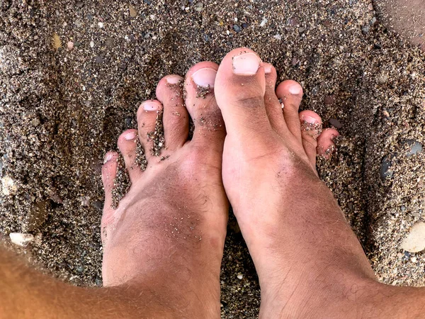 Closeup of male feet resting on a sandy beach