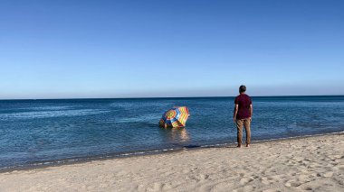 A man standing on the beach and watching his parasol sinking in the Mediterranean sea