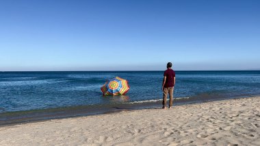 A man standing on the beach and watching his parasol sinking in the Mediterranean sea