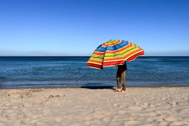 A man holding an open parasol on the beach