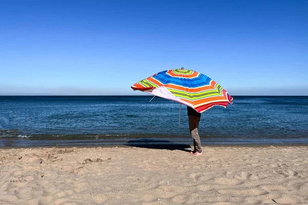 A man holding an open parasol on the beach