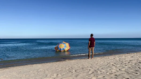 A man standing on the beach and watching his parasol sinking in the Mediterranean sea