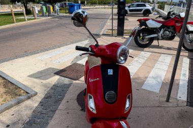 Kırmızı Vespa scooter 'ı deniz manzaralı caddeye park etmiş.