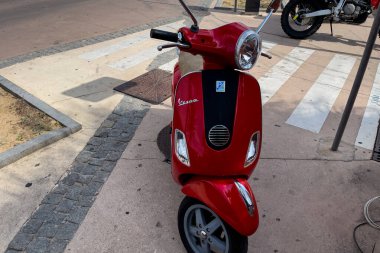 Kırmızı Vespa scooter 'ı deniz manzaralı caddeye park etmiş.