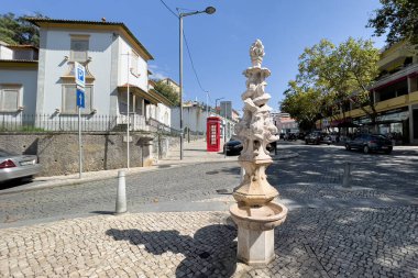 Sintra 'da kaldırımda arkasında kırmızı telefon kulübesi olan bir çeşme.