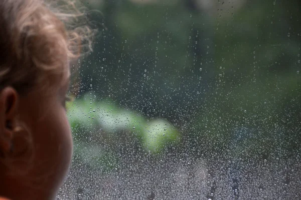 Rain drops on the surface of a window pane with a blurred silhouette of a girl. Natural pattern of raindrops on a natural background and the silhouette of a child