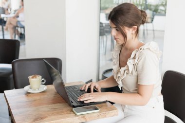 Bilgisayarla çalışırken kahve içen genç bir kadın.