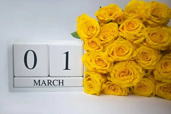 Calendrier en bois le 1er mars et roses jaunes sur fond blanc. — Photo