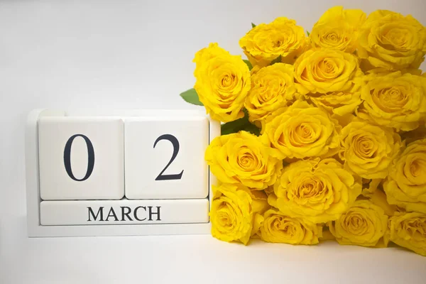 Calendrier en bois le 2 mars et roses jaunes sur fond blanc. — Photo