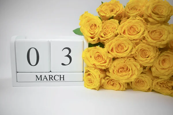 Calendrier en bois le 3 mars et roses jaunes sur fond blanc. — Photo