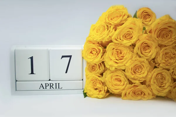 Calendrier en bois le 17 avril et roses jaunes sur fond blanc. — Photo