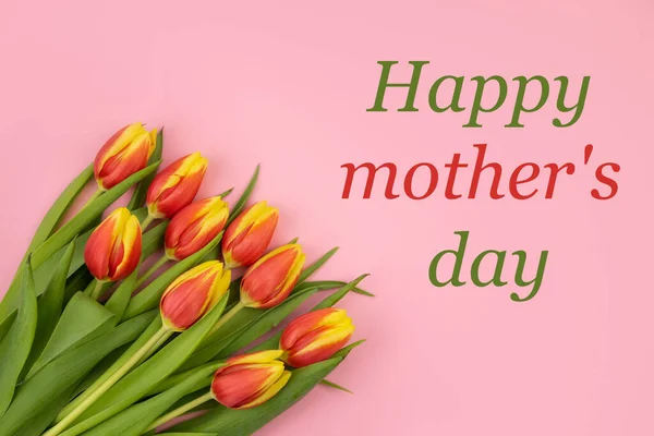 Laleler sarı-kırmızıdır, pembe bir zemin üzerinde ve "Mutlu Anneler Günü" yazısı.. — Stok fotoğraf