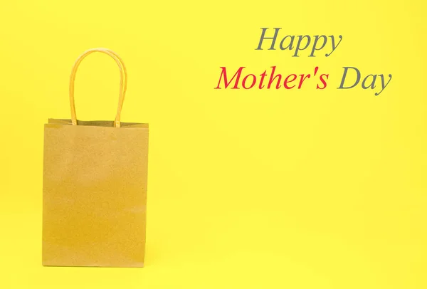 A paper bag with the words Happy Mothers Day , in gray and red, on a yellow background.