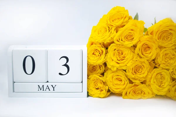 3 mai sur un calendrier blanc en bois et un bouquet jaune de roses côte à côte — Photo