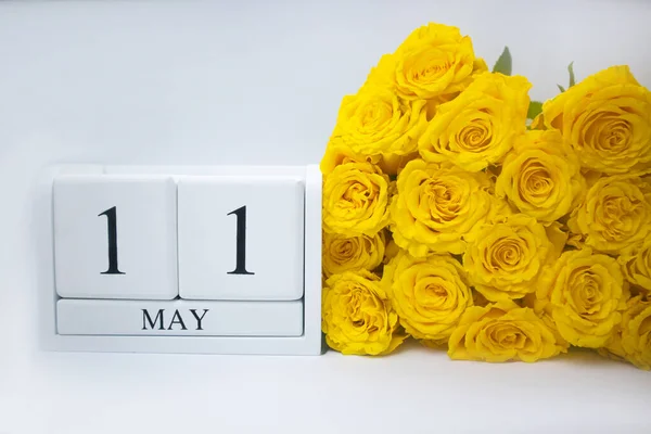 11 de mayo en un calendario de madera blanca y un ramo amarillo de rosas se encuentran lado a lado —  Fotos de Stock