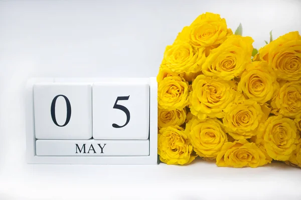 5 mei op een witte houten kalender en een geel boeket rozen liggen zij aan zij — Stockfoto