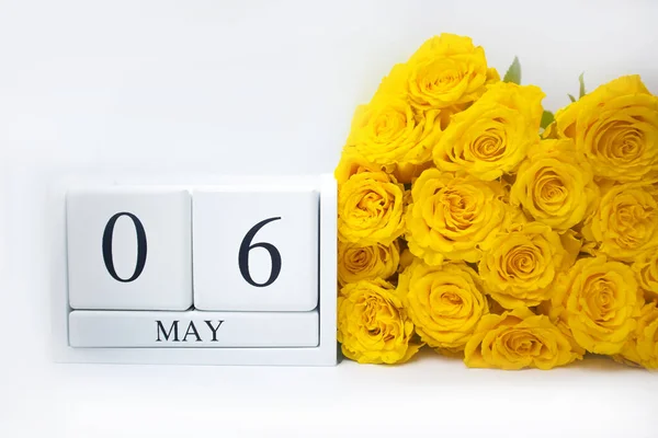 6 mei op een witte houten kalender en een geel boeket rozen liggen zij aan zij. — Stockfoto