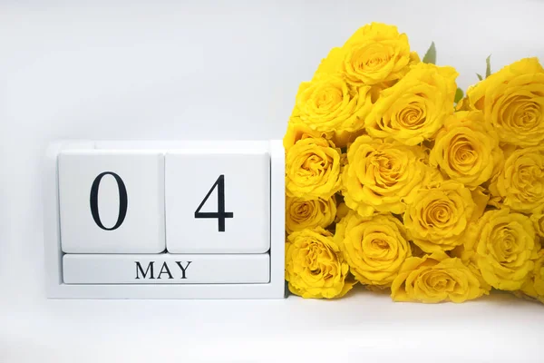 4 mei op een witte, houten kalender en een geel boeket rozen liggen zij aan zij — Stockfoto