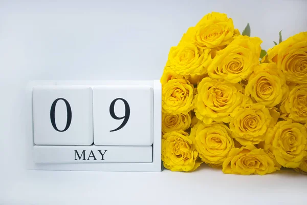 9 mei op een witte houten kalender en een geel boeket rozen liggen zij aan zij. — Stockfoto