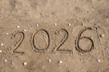 2026 rakamları el yazısıyla kumsalda, deniz kıyısında, kabuğun etrafında yazılır. Tatil konsepti, tatiller, yeni yıl, turizm, reklam, seyahat. Yüksek kalite fotoğraf