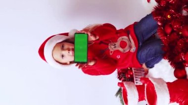 Noel zamanı. Küçük bir kız elinde yeşil ekranlı, Noel Baba şapkalı, kırmızı kazaklı, süslü püslü ve taşaklı bir telefon tutuyor. Kavram reklamcılığı, teknoloji, duyuru, tebrikler, davetiyeler, modeller. 
