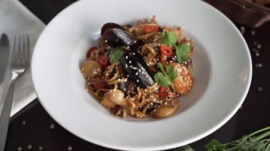 Beyaz tabakta süslenmiş deniz ürünleri makarnası.