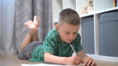 Okul çocuğu ödevini yapıyor. Çocuk odasında yerde yatıyor.