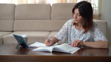 Beautiful woman reading a book in the living room, drinks coffee and works with a tablet