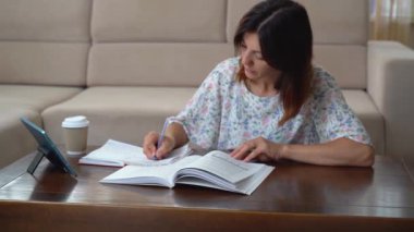 Bir kadın tabletten bir video izler ve not defterine not alır.