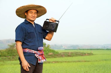 Asyalı çiftçi çeltik tarlasında, telsiz alıcısı beklemede. Konsept: Müzikle birlikte çalışmaktan mutluyum. Taşra yaşam tarzı. Bilgi, bilgi, haber, reklam almak, radyodan şarkılar dinlemek.
