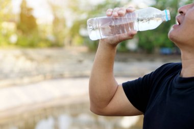 Asyalı adamın portresi açık hava parkında şişeden su içiyor. Sağlıklı yaşam tarzı kavramı. Sağlık için su iç..        