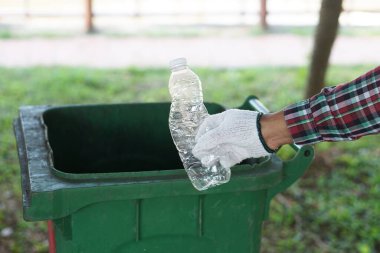Eldiven takıyor, parktaki çöp kutusuna atmak için plastik şişe tutuyor. Konsept: çöpleri geri dönüşümle ayıklamak. Plastik çöpleri geri dönüştür. Atık yönetimi.     