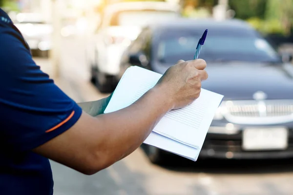 Selective focus on hand of car insurance agency  is writing about details of car broken from accident on paper. Blurred car background. Concept : insurance service.