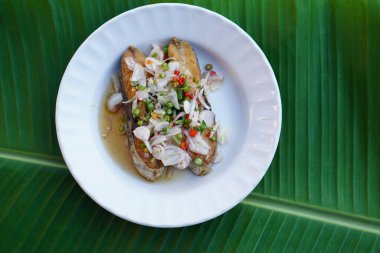 Kızarmış Kral uskumru salatası, beyaz tabakta. Kavram: aşçılık. Deniz ürünleri. Taylandlıların pirinçle yediği lezzetli menü ve tuzlu balıklı menü. Tayland mutfağı. Muz yaprağı arkaplanı