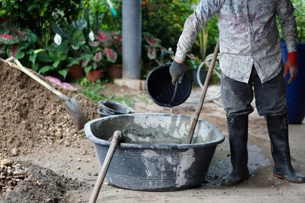 Adam işçi elle inşaat alanında çalışıyor, kovayı tutuyor, çimento tozu, kum ve taşları karıştırmak için bir çapa kullanıyor. Konsept: inşaat işçisi. Sıkı çalışma..            