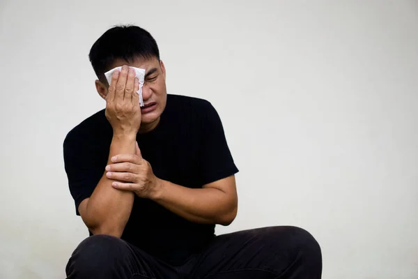 Portrait of Asian man feels hurt, use white tissue paper to cover his eye. Concept : health problems. Man cry, emotional expression.