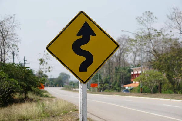 Yellow traffic sign  with twisty arrow symbol at rural road Thailand to warn drivers be careful when driving on twisty way road. Concept : Warning traffic sign for transportation.