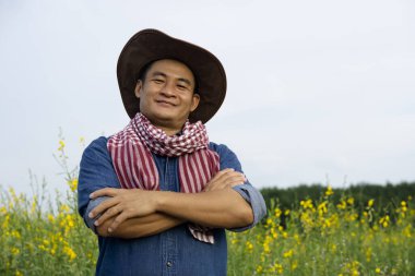 Yakışıklı Asyalı çiftçinin portresi bahçede, şapka ve mavi gömlek giyiyor, kolları göğsünde çapraz, kendinden emin, kameraya bakıyor. Kavram: Tarım işgali.