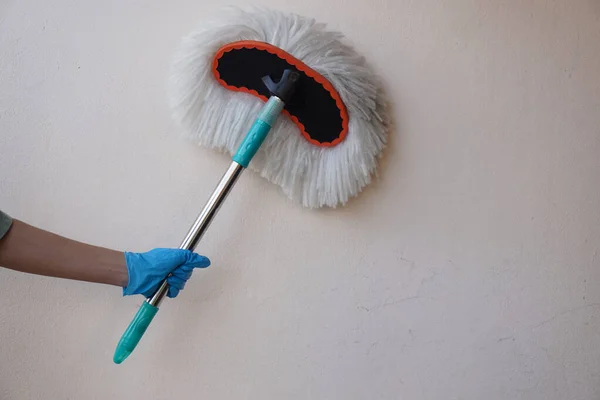 Closeup hand wears protective rubber glove, holds dust mop to clean the wall.  Concept : Cleaning, daily household chore.