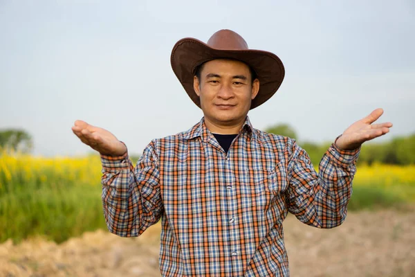 Handsome  Asian man farmer wears hat and plaid shirt, makes hands gesture to present something, feels confident.  Concept : Agriculture occupation.  Copy space for adding text or advertisement.