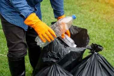 Closeup garbage collector worker hands hold plastic bottles to put into black garbage bags to recycle. Concept : Environment conservation. Waste management. Cleaning public place activity. 