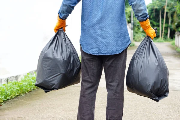 Closeup man holds black plastic bag that contains garbage inside. Concept : Waste management. Environment problems. Daily chores. Throw away rubbish.