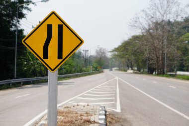 Tayland kırsal yolundaki sol dar şerit tabelasında sarı trafik meydanı. Sürücünün sol taraftaki dar yolları bildiğini gösteriyor. Kavram: Uyarı trafik uyarısı.           